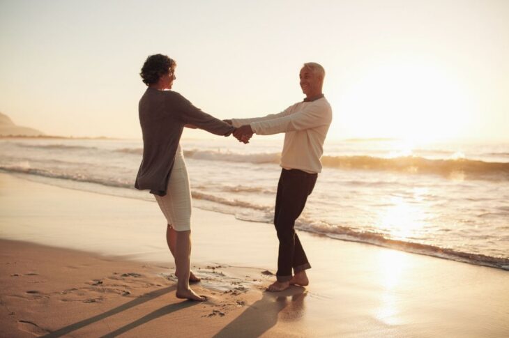 Full length outdoor shot of senior couple holding hands standing on the beach